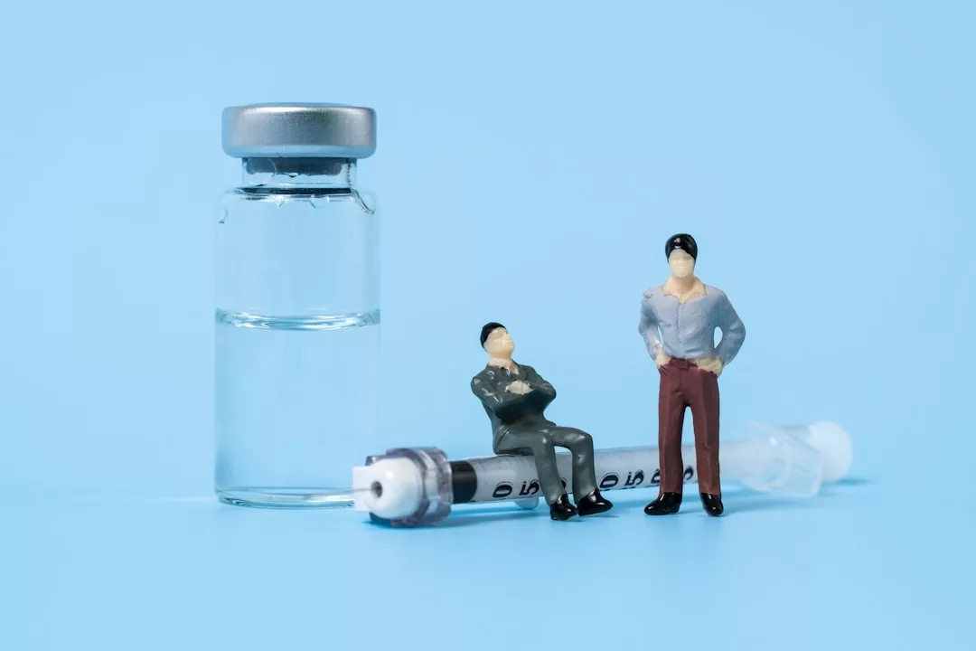 Ein Fläschchen, eine Spritze und zwei Miniaturfiguren von Menschen sind vor einem hellblauen Hintergrund angeordnet und unterstreichen den innovativen Ansatz von GLAMESiA.