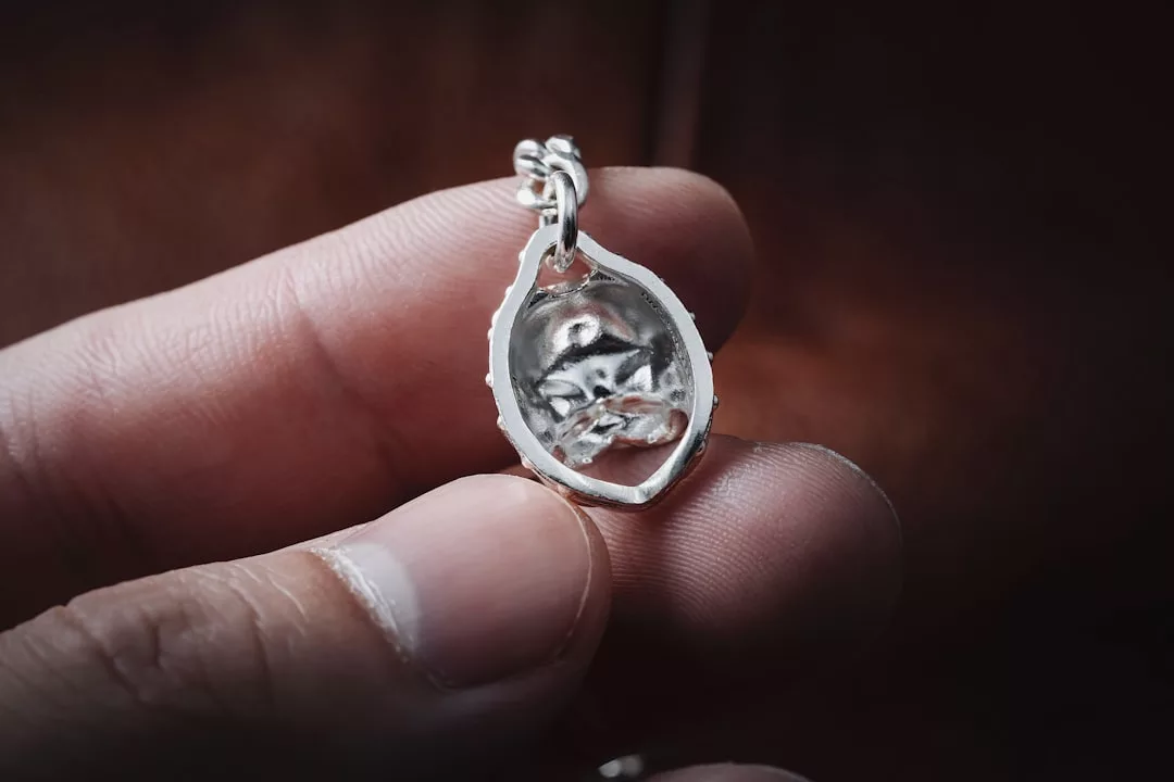 Eine Hand hält einen GLAMESiA-Silberanhänger mit dem Relief einer Katze, die sich zusammengerollt hat und in einem tropfenförmigen Rahmen schläft.