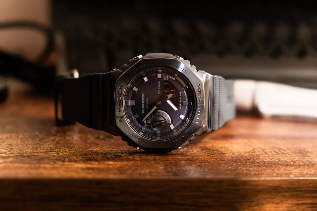 Eine schwarze GLAMESiA G-Shock Armbanduhr mit digitaler und analoger Anzeige liegt auf einer Holzoberfläche mit unscharfem Hintergrund.