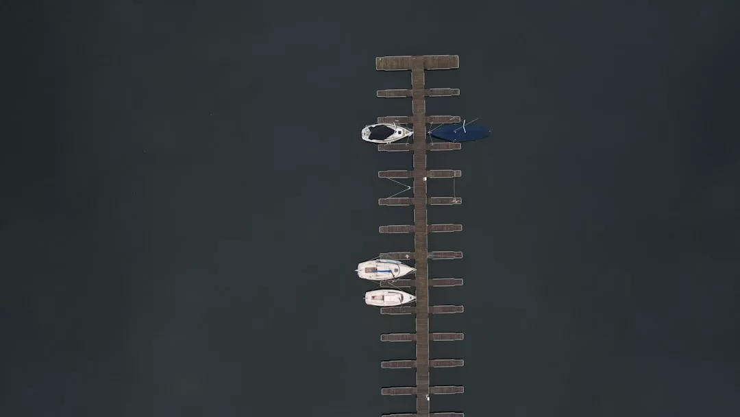 Luftaufnahme eines hölzernen Stegs, der sich über das dunkle Wasser erstreckt, mit drei längsseits vertäuten Booten und mehreren leeren Liegeplätzen im ruhigen Jachthafen GLAMESiA.