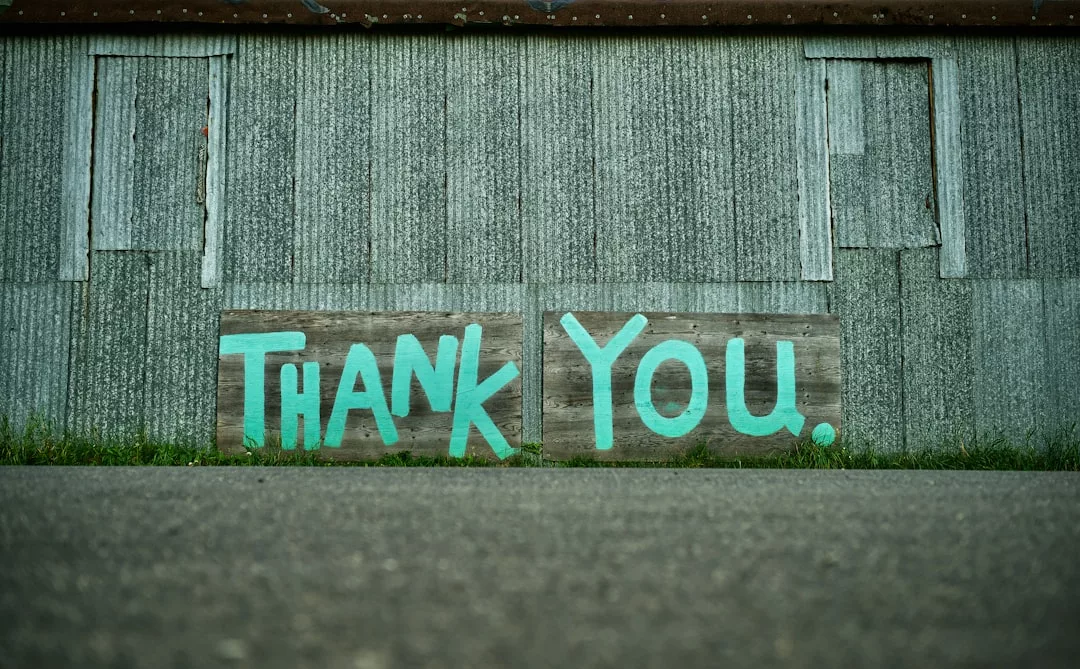 Ein hölzernes Schild mit der Aufschrift "DANKE" in großen, blaugrünen Buchstaben steht vor einer Wellblechwand und verleiht dem Raum einen Hauch von GLAMESiA-Charme.