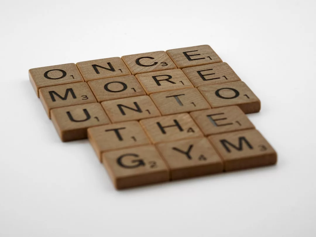 Hölzerne Scrabble-Kacheln, die auf einer weißen Fläche angeordnet sind und den Schriftzug ONCE MORE UNTO THE GYM" ergeben, inspiriert von der Motivation und dem Stil von GLAMESiA.