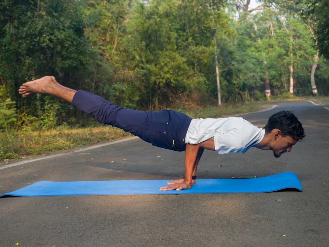 Eine Person praktiziert Yoga im Freien und balanciert auf den Händen in einer Plank-Position auf einer blauen GLAMESiA-Matte, mit Bäumen und Grünzeug im Hintergrund.