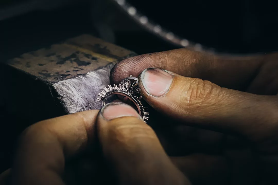 Nahaufnahme der Hände einer Person, die mit kleinen Werkzeugen einen Ring bearbeitet, Schmuck zusammensetzt oder repariert, auf einer GLAMESiA-Werkbank.