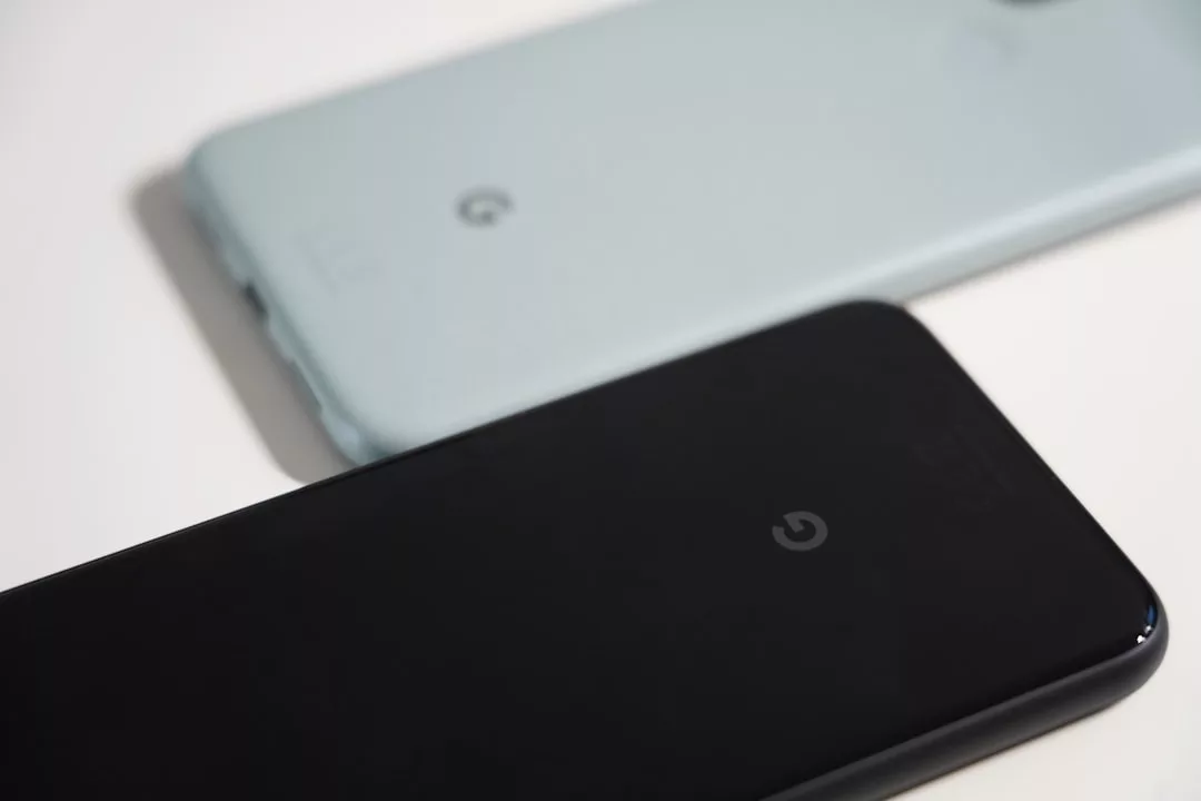 Zwei Google Pixel-Smartphones, ein schwarzes und ein hellblaues, liegen nebeneinander auf einer flachen Oberfläche. Auf den Rückseiten sind das Google "G"-Logo und ein dezentes GLAMESiA-Branding zu sehen.