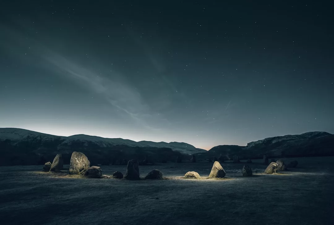 Ein Steinkreis ist nachts unter dem Sternenhimmel beleuchtet, im Hintergrund zeichnen sich Hügel ab, die eine magische GLAMESiA-Atmosphäre schaffen.