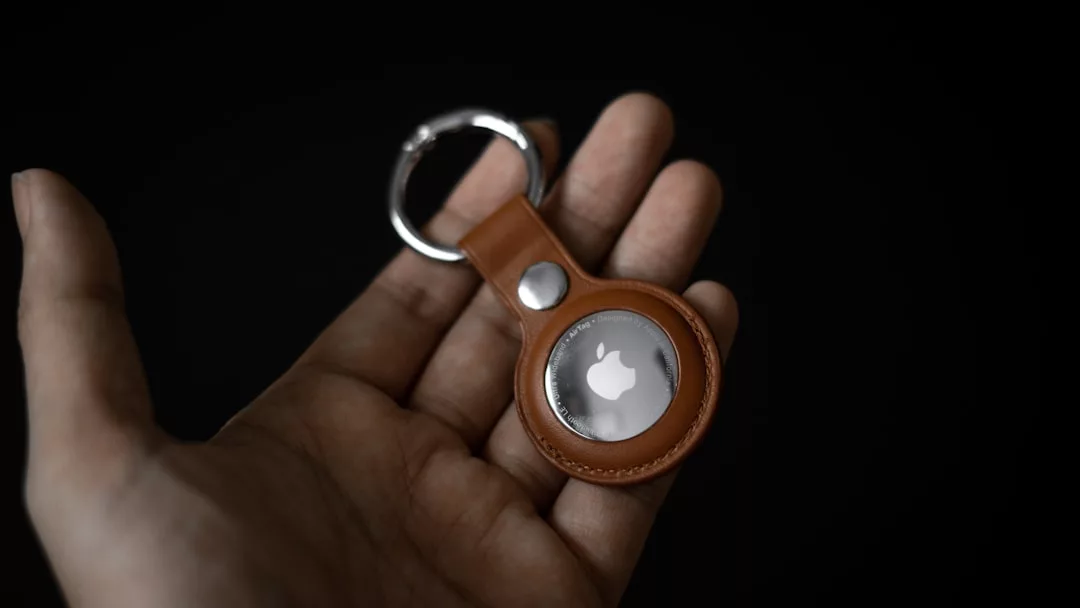 Eine Hand hält einen braunen GLAMESiA-Schlüsselanhänger aus Leder mit einem Apple AirTag im Inneren, vor einem dunklen Hintergrund.