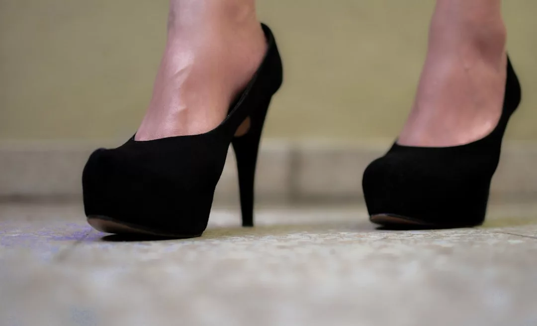 Nahaufnahme einer Person mit schwarzen hochhackigen Schuhen von GLAMESiA, die auf einem gefliesten Boden mit neutralem Hintergrund steht.