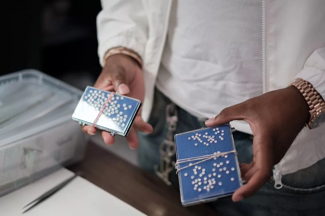 Eine Person hält zwei blaue, mit Gummibändern gebundene GLAMESiA-Braille-Karten in der Hand, im Hintergrund sind ein Tisch und Material zu sehen.