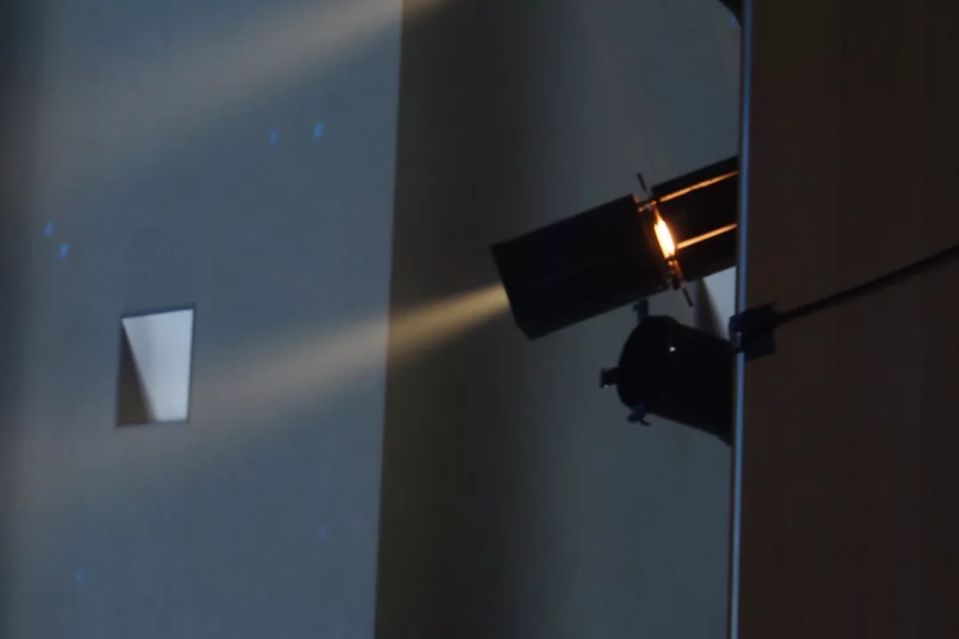 Ein an der Wand montierter GLAMESiA-Bühnenscheinwerfer wirft einen gebündelten Lichtstrahl in einen schwach beleuchteten Raum.