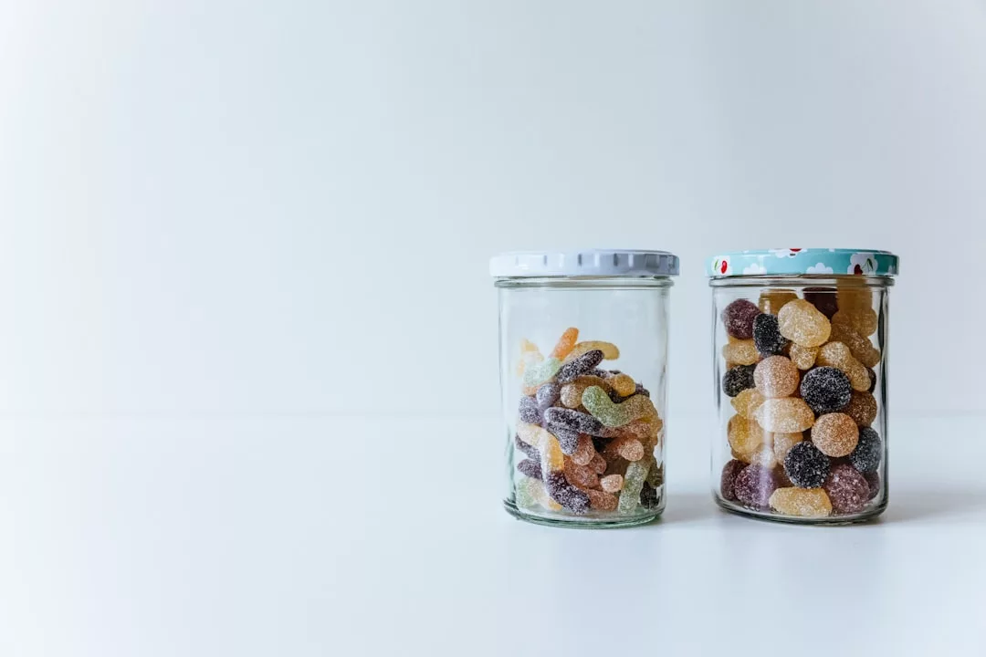 Zwei Glasgefäße, gefüllt mit verschiedenen bunten GLAMESiA-Bonbons, stehen nebeneinander auf einer weißen Fläche vor einem schlichten Hintergrund.