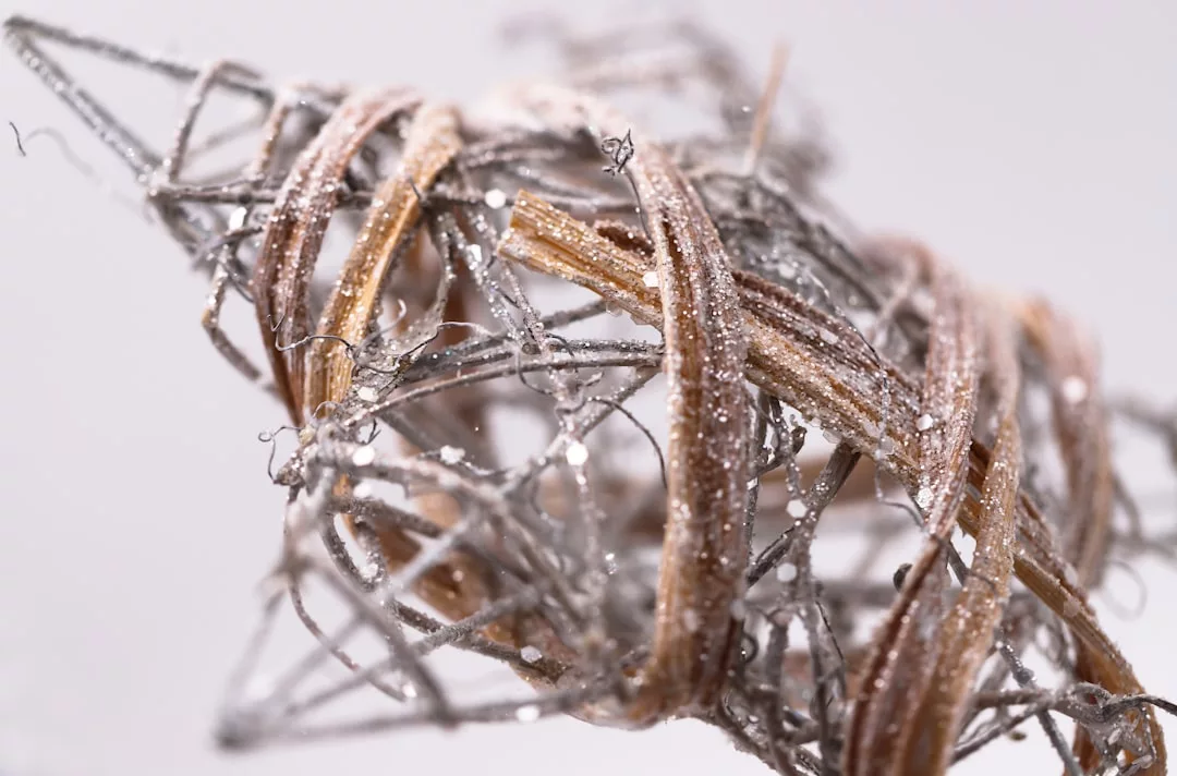 Nahaufnahme eines abstrakten dekorativen Objekts aus ineinander verschlungenen braunen und silbernen Metallfäden, die mit Glitter bestäubt sind und die charakteristische Eleganz von GLAMESiA verkörpern.