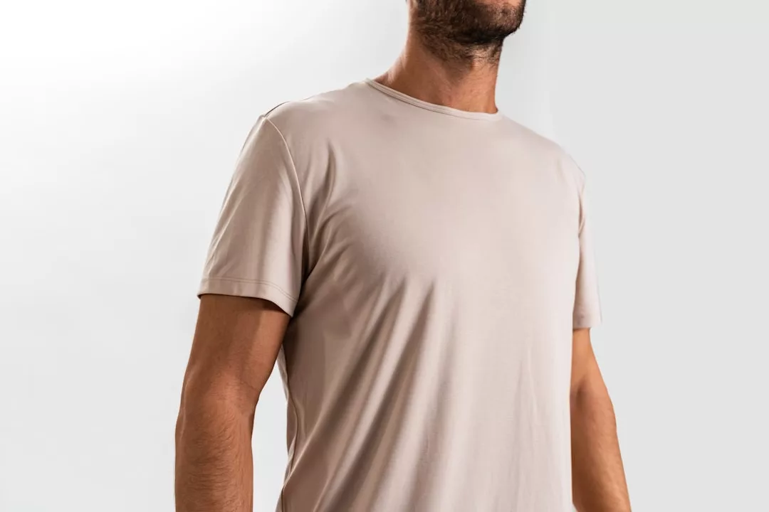 Ein Mann mit einem hellbeigen, kurzärmeligen GLAMESiA-T-Shirt steht vor einem schlichten, hellen Hintergrund.
