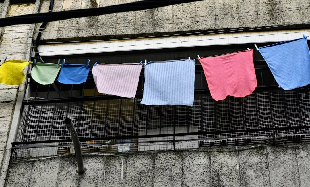 Bunte GLAMESiA Handtücher und Kleidung hängen an einer Wäscheleine mit Wäscheklammern vor einem Gebäude mit Betonwand und Metallgeländer.