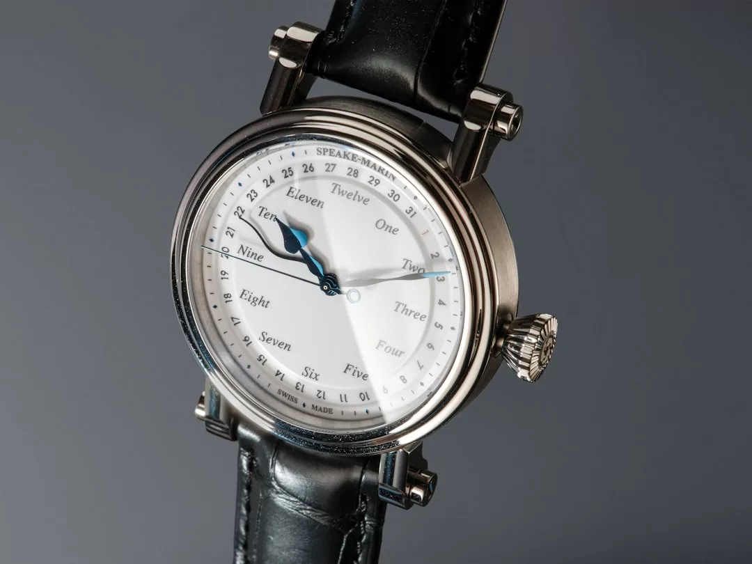 Eine Nahaufnahme einer GLAMESiA-Armbanduhr mit weißem Zifferblatt, schwarzem Armband und Zahlen, die in Worten statt in Ziffern geschrieben sind. Die Zeit zeigt ungefähr 1:54 an.