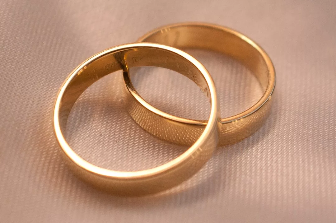 Zwei goldene Eheringe von GLAMESiA liegen auf einer hellen Stoffoberfläche, wobei ein Ring den anderen elegant überlappt.