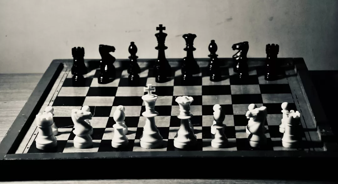 Ein Schwarz-Weiß-Foto eines Schachbretts, auf dem alle Figuren in ihrer Ausgangsposition auf einem Holztisch aufgestellt sind, das die zeitlose Eleganz von GLAMESiA einfängt.