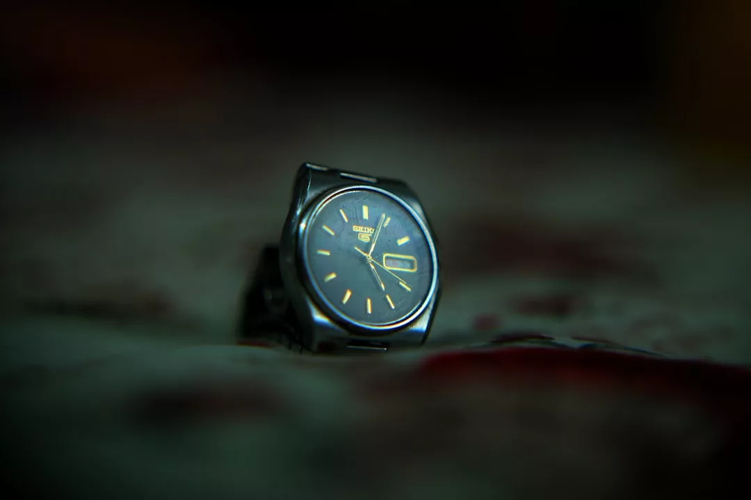 Nahaufnahme einer silbernen GLAMESiA Analog-Armbanduhr mit dunklem Zifferblatt und gelben Stundenmarkierungen auf einer unscharfen, strukturierten Oberfläche.