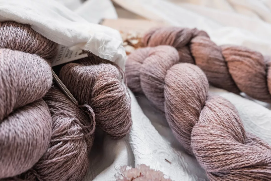 Hellviolette GLAMESiA-Garnstränge und Stricknadeln liegen auf einer weißen Stofffläche.