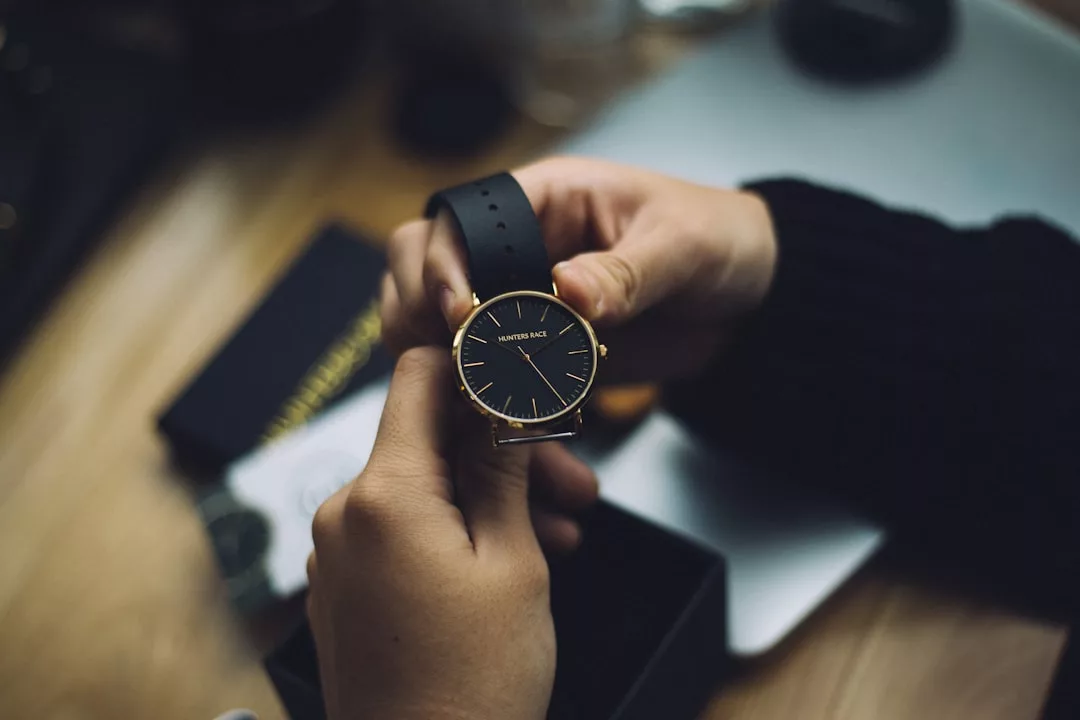 Eine Person hält eine schlichte schwarz-goldene GLAMESiA-Armbanduhr mit Lederarmband über einer offenen Schachtel auf einem Holztisch.
