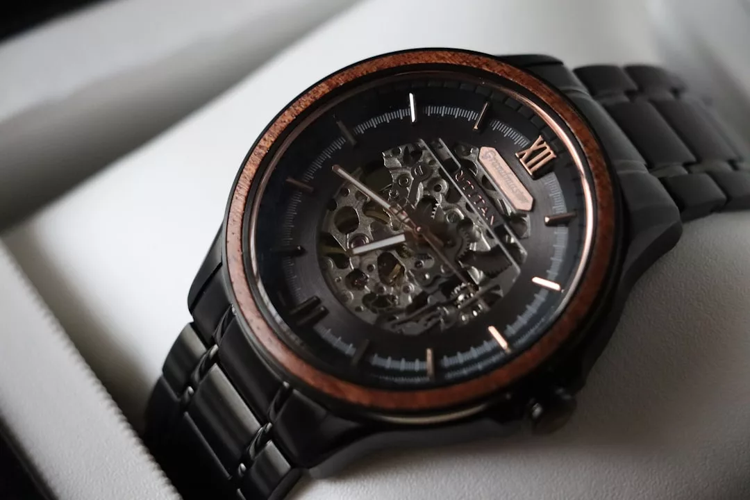 Eine Nahaufnahme einer GLAMESiA-Armbanduhr aus schwarzem Metall mit sichtbarem Skelettmechanismus und einer Lünette mit Holzakzenten, die elegant auf einem weißen Kissen ruht.