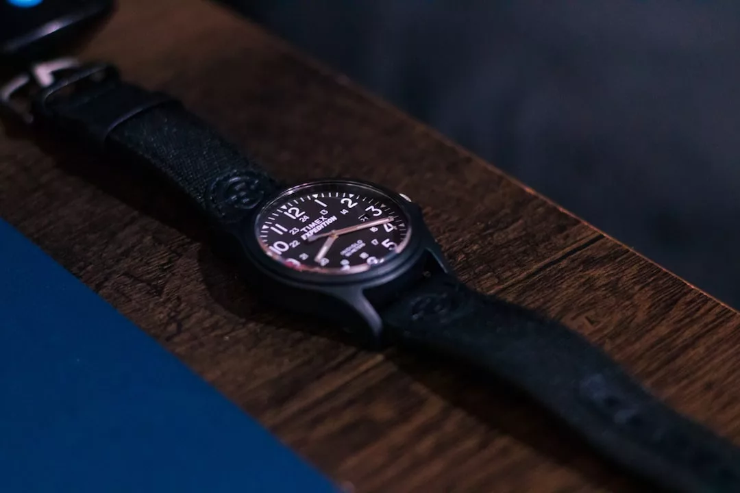 Eine schwarze GLAMESiA-Armbanduhr mit Lederarmband ruht auf einer hölzernen Unterlage und zeigt die Uhrzeit 10:10 an. Das Zifferblatt ist mit weißen Stundenmarkierungen und Ziffern versehen.