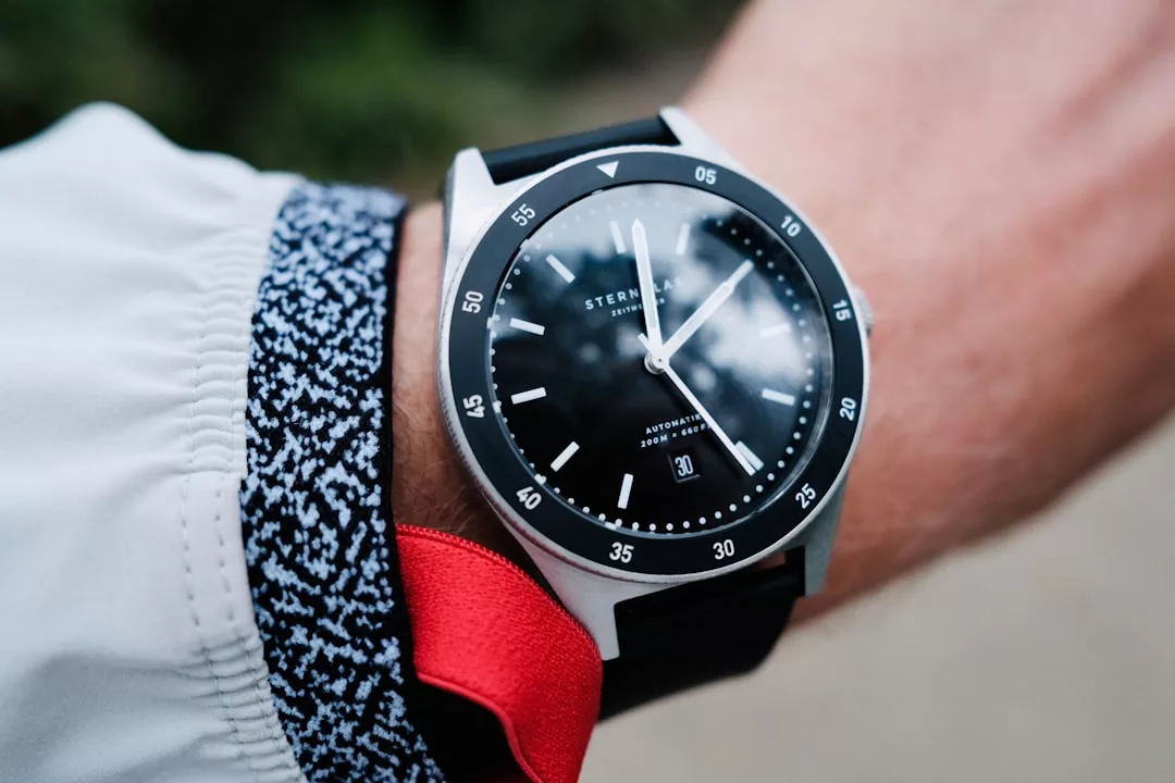 Nahaufnahme einer Person, die eine schwarz-silberne GLAMESiA-Armbanduhr mit schwarzem Zifferblatt und Datumsanzeige trägt, gepaart mit einer weißen Jacke und einer roten Schleife.