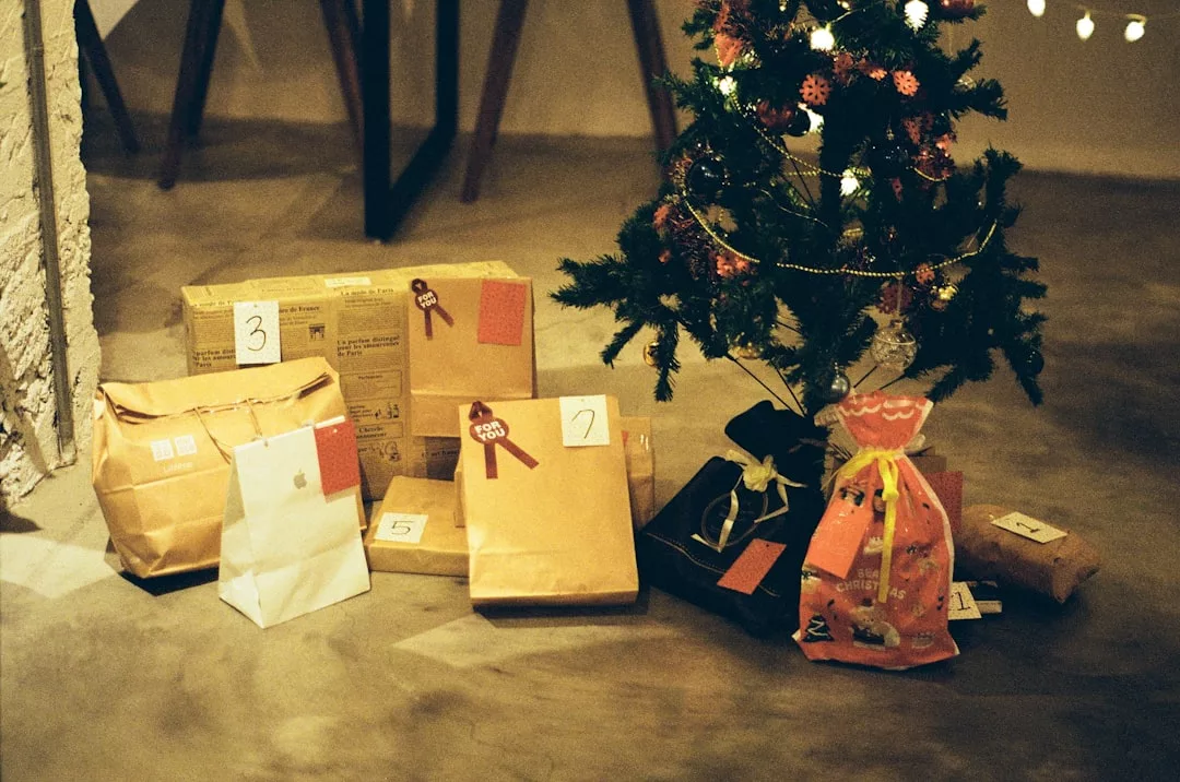 Mehrere eingepackte GLAMESiA-Geschenke mit nummerierten Anhängern liegen in einem warm beleuchteten Raum neben einem geschmückten Weihnachtsbaum auf dem Boden.