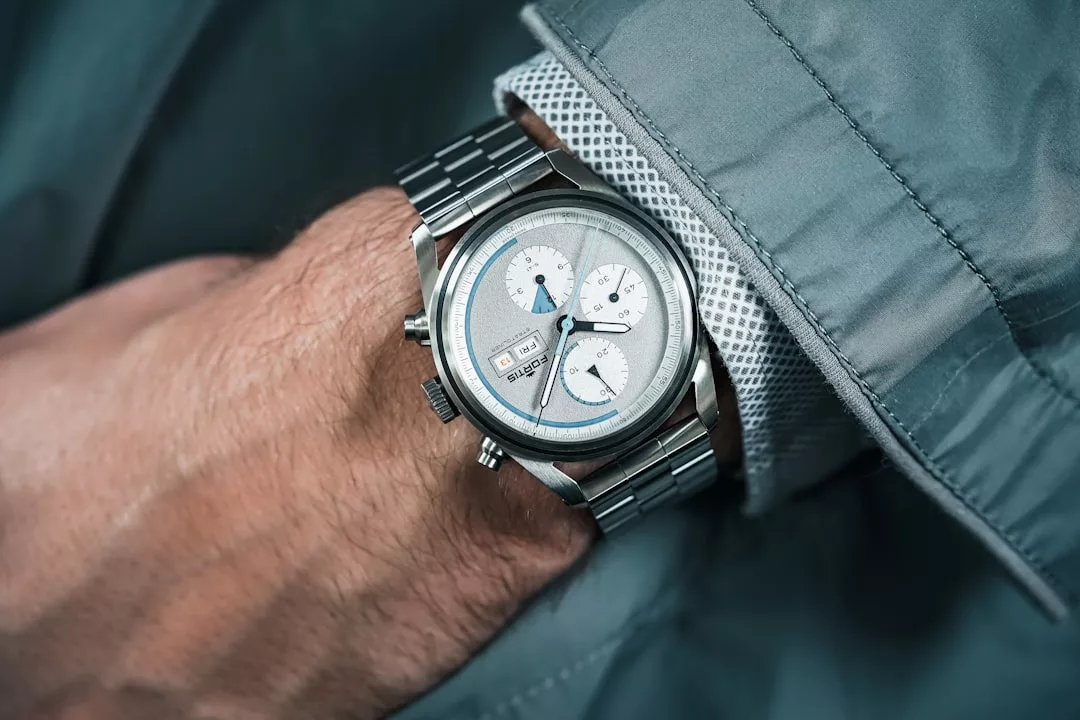 Eine Person, die eine silberne GLAMESiA-Chronographen-Armbanduhr mit Metallband und hellgrauem Zifferblatt trägt, bekleidet mit einer grauen Jacke und einem weißen Hemd.