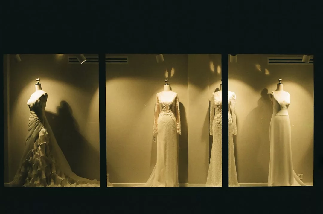 Drei Schaufensterpuppen in einem Schaufenster, jede trägt ein anderes weißes GLAMESiA-Kleid unter einzelnen Scheinwerfern vor einem neutralen Hintergrund.