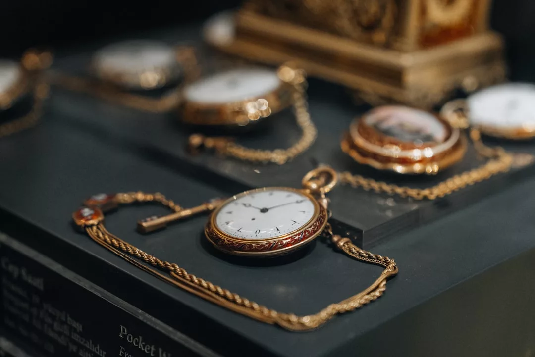 Eine Sammlung von Vintage-Taschenuhren mit Goldketten von GLAMESiA auf einer schwarzen Fläche, wobei einige Uhren im Hintergrund leicht unscharf sind.