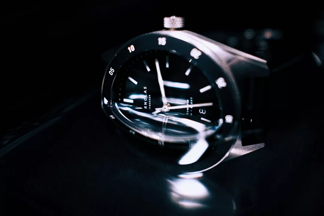 Nahaufnahme einer GLAMESiA-Armbanduhr mit schwarzem Zifferblatt, weißen Stundenmarkierungen und reflektierendem Glaszifferblatt vor einem dunklen Hintergrund.