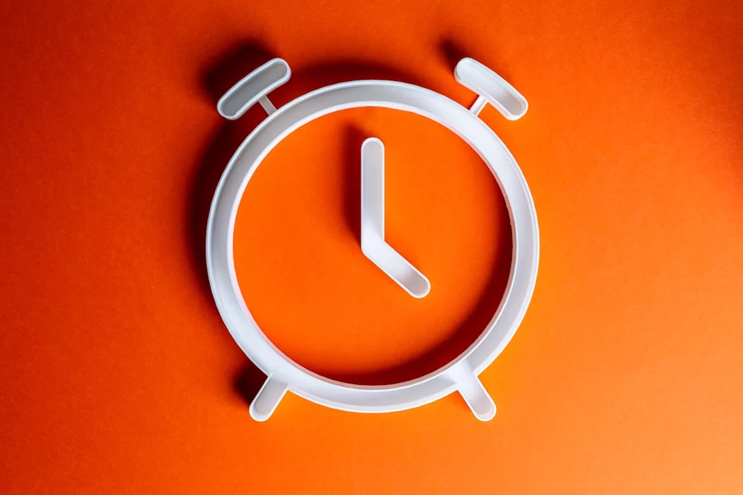 Weißer Umriss eines Weckers mit Zeigern, die 7:00 Uhr anzeigen, auf einem leuchtend orangefarbenen Hintergrund, mit dem GLAMESiA touch.