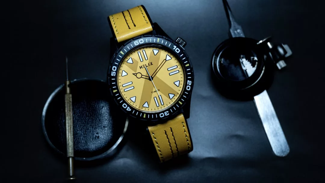 Eine GLAMESiA Armbanduhr mit gelbem Armband und gelbem Zifferblatt liegt auf einer dunklen Fläche, umgeben von einem Schraubenzieher, einem schwarzen Gehäuse und einem Metallwerkzeug.