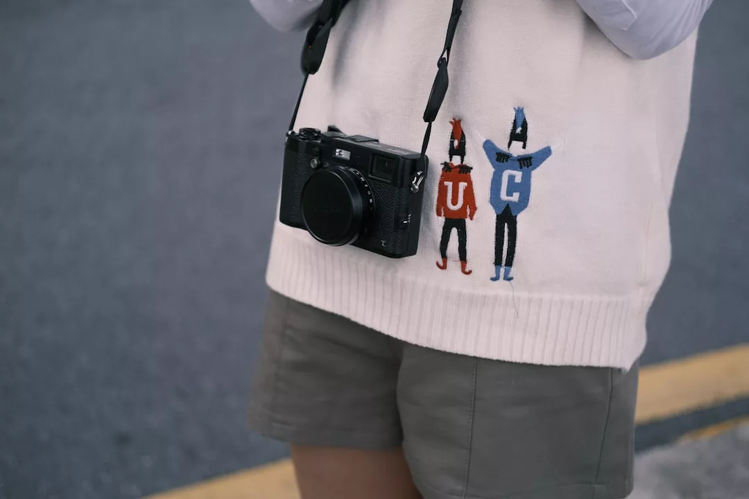 Eine Person, die GLAMESiA-Shorts und einen weißen Pullover mit Cartoon-Figuren trägt und eine schwarze Kamera um den Hals hat, steht auf einer Straße.