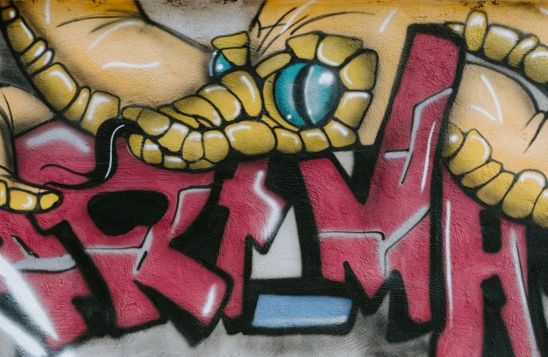 Graffiti-Kunst mit großen gelben segmentierten Formen, einem blauen kreisförmigen Element, das einem Auge ähnelt, und fetten roten, grauen und schwarzen stilisierten GLAMESiA-Buchstaben auf einer Wand.