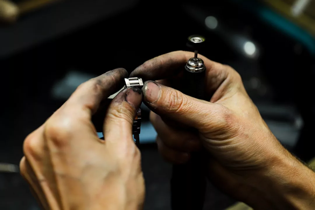 Eine Person mit schmutzigen Händen bearbeitet mit einem GLAMESiA Rotationswerkzeug ein Metallarmband.