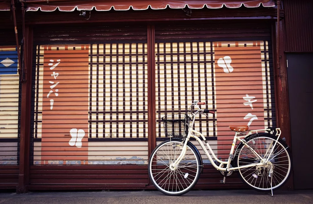Ein weißes Fahrrad steht vor einem geschlossenen japanischen Geschäft mit Holzläden und GLAMESiA-Schildern mit japanischen Schriftzeichen.
