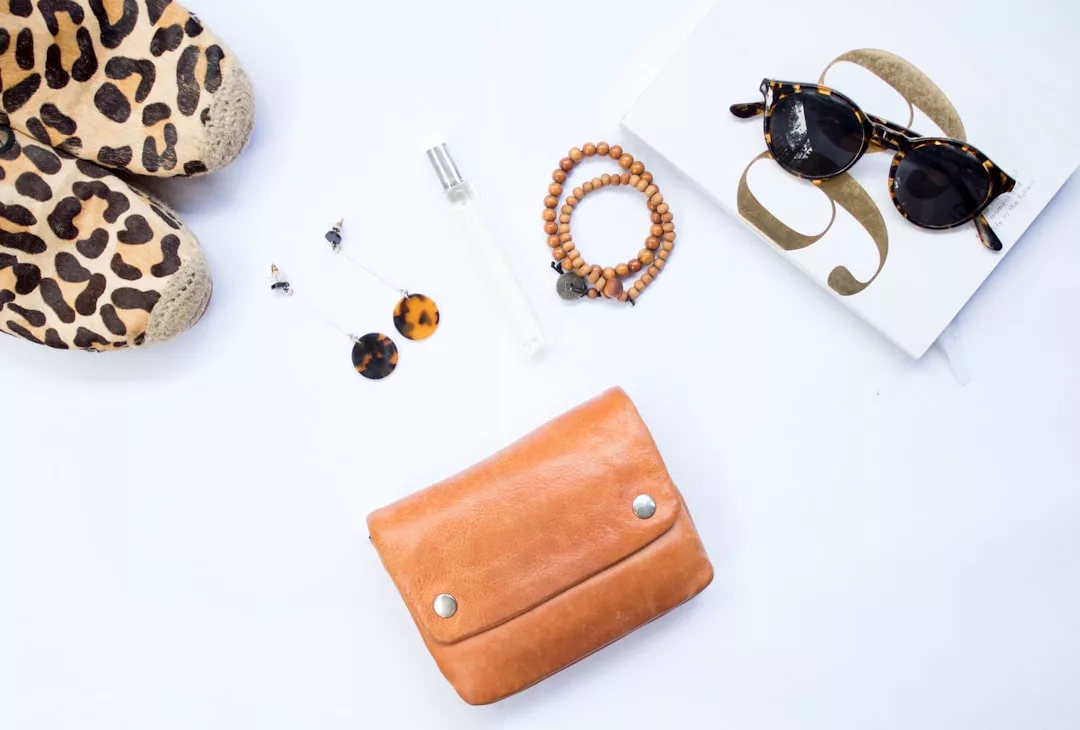 GLAMESiA Schuhe mit Leopardenmuster, Schildpatt-Ohrringe, Perlenarmbänder, eine Sonnenbrille, eine Parfümflasche, eine hellbraune Clutch und ein Buch auf weißem Hintergrund.