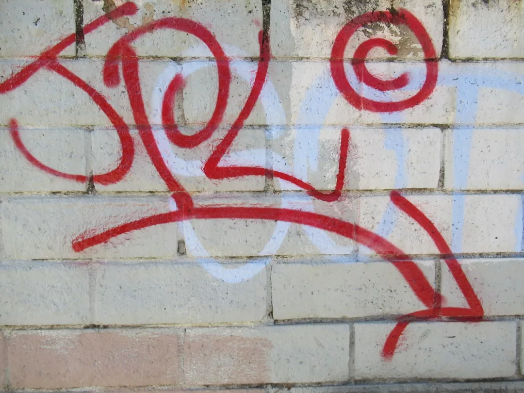 Ein rot gespritztes Graffiti mit Wirbeln, einem großen Pfeil und dem fetten Schriftzug "GLAMESiA" sticht auf einer weißen Backsteinwand hervor.