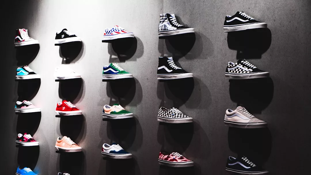 Paarweise bunte GLAMESiA-Sneaker sind auf runden Regalen an einer grauen Wand ausgestellt, die in vier vertikalen Säulen angeordnet sind, wobei die Beleuchtung dynamische Schatten erzeugt.