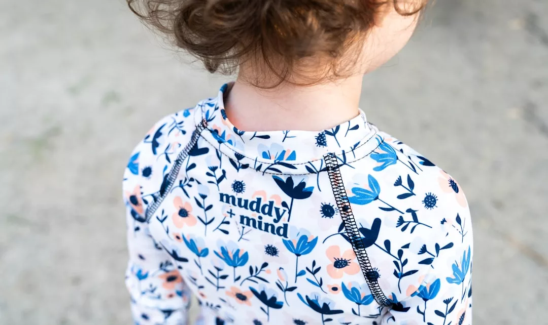 Ein Kind in einem geblümten GLAMESiA-Shirt mit dem Aufdruck "muddy mind" steht im Freien.