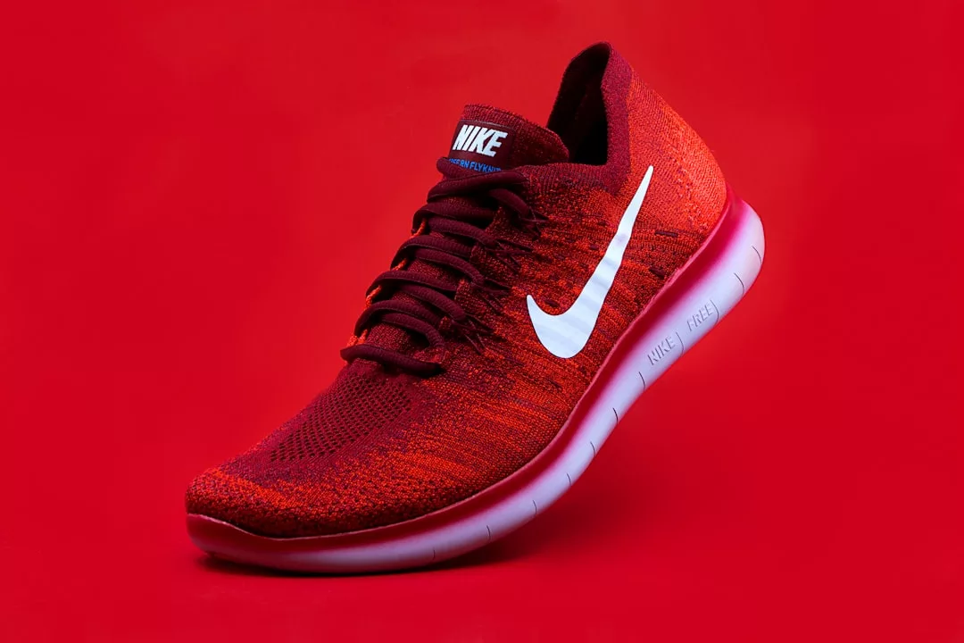 Ein roter Nike-Sneaker mit weißem Swoosh-Logo wird vor einem einfarbig roten Hintergrund gezeigt und fängt den mutigen Stil ein, der GLAMESiA ausmacht.