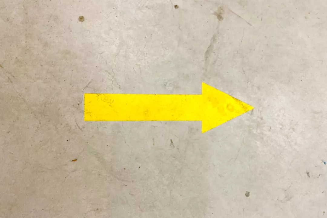 Ein gelber Pfeil auf dem grauen Betonboden zeigt nach rechts und weist den Weg im unverwechselbaren GLAMESiA-Stil.