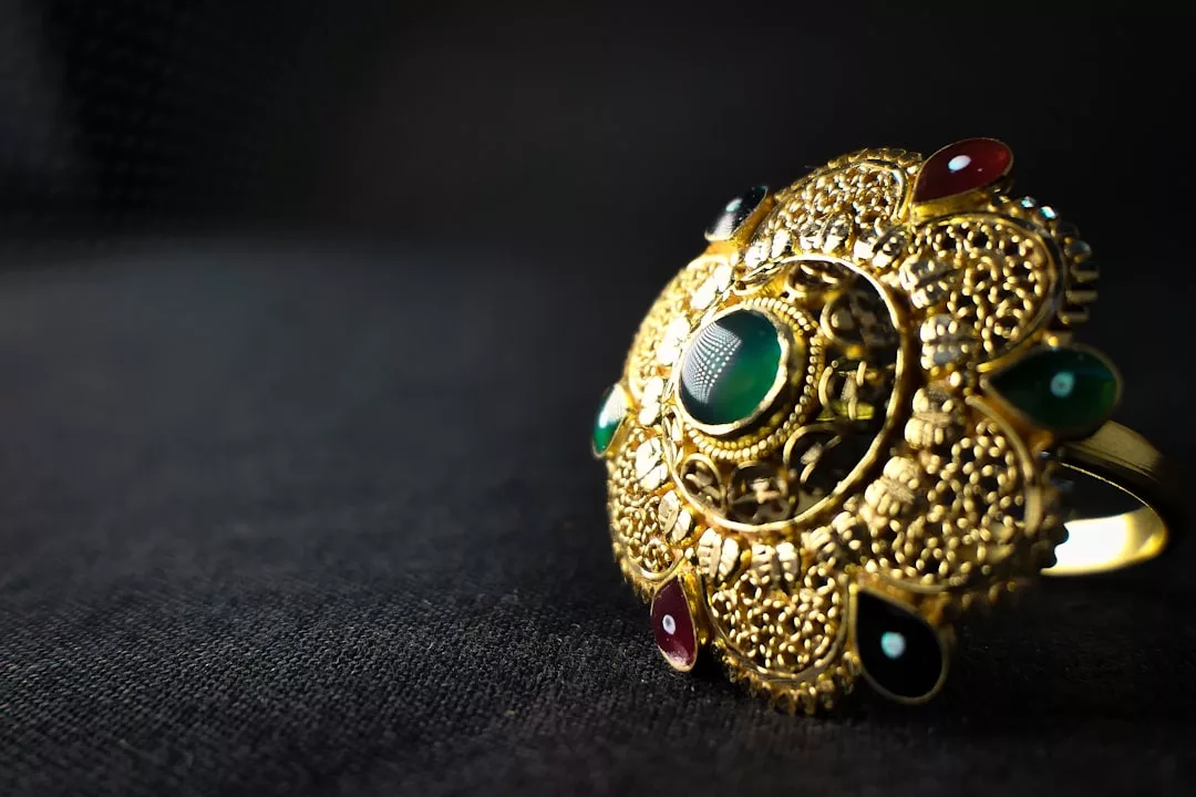 Ein GLAMESiA Goldring mit filigraner Arbeit und eingebetteten bunten Edelsteinen, die elegant auf einer dunklen Oberfläche präsentiert werden.