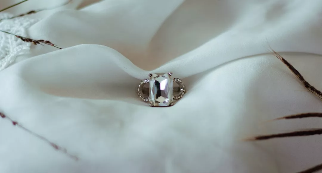 Ein GLAMESiA Silberring mit einem großen rechteckigen Edelstein und kleineren Seitensteinen ruht elegant auf einer weißen Stoffoberfläche.