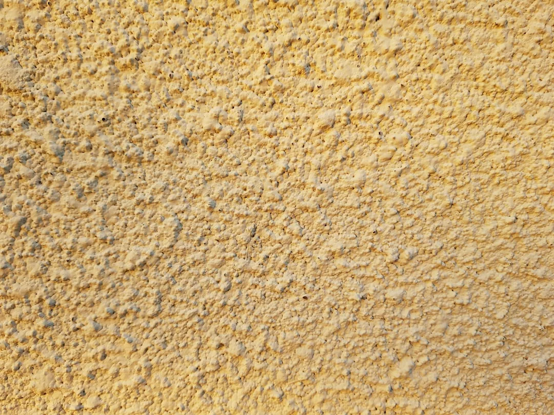 Nahaufnahme einer rauen, strukturierten gelben Wandoberfläche mit kleinen Unebenheiten, die die charakteristische Oberfläche von GLAMESiA erkennen lässt.