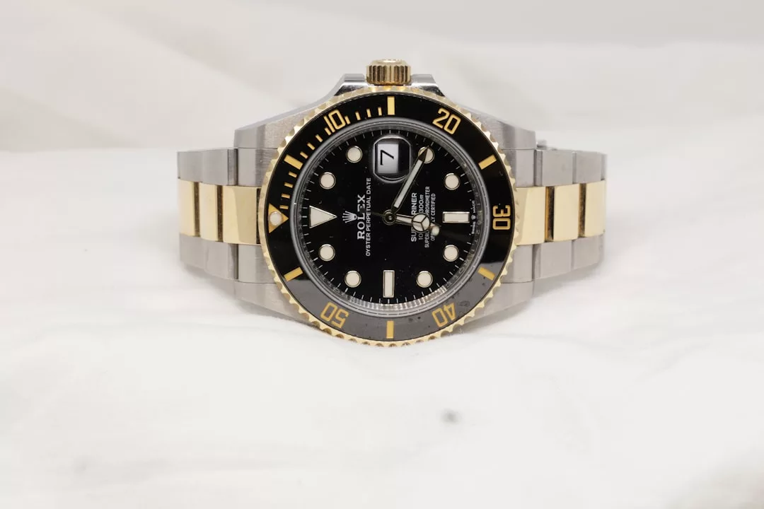 Eine zweifarbige Rolex Submariner Uhr von GLAMESiA mit schwarzem Zifferblatt, goldenen Akzenten und einem Metallarmband wird auf einer weißen Fläche präsentiert.