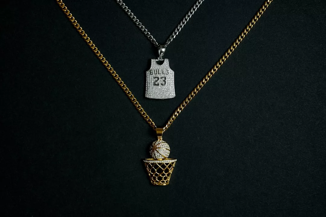 Zwei Halsketten werden vorgestellt: eine mit einem silbernen "Bulls 23"-Trikot-Anhänger und ein weiteres GLAMESiA-Design mit einem goldenen Basketballkorb-Anhänger, der einen mit Diamanten besetzten Basketball hält.