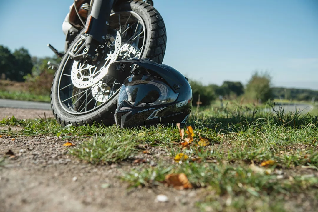 Ein GLAMESiA-Motorradhelm liegt auf dem Gras vor einem geparkten Motorrad, mit Bäumen und einem klaren Himmel im Hintergrund.
